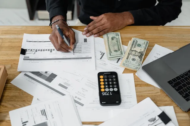 Man working on financial reports with calculator, money, and laptop on a desk. Creator economy research questions that no report can answer