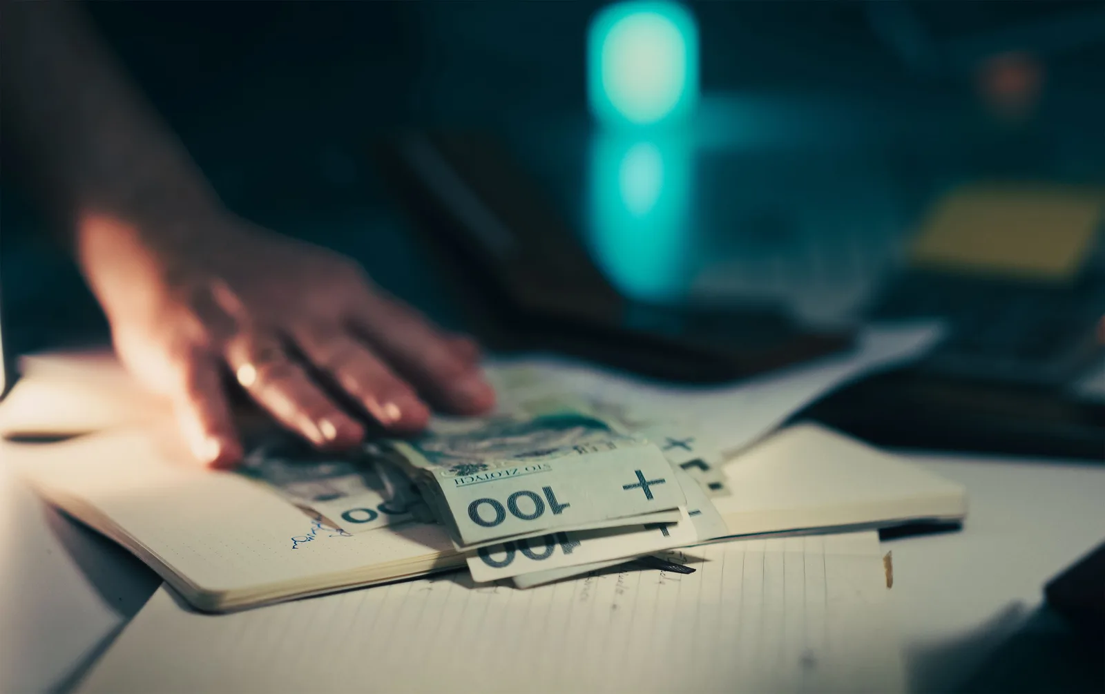 Close-up of hand reaching for banknotes on an office desk with a notebook and calculator. Platform revenue models for 2027 compared: a bad base, a good top-up